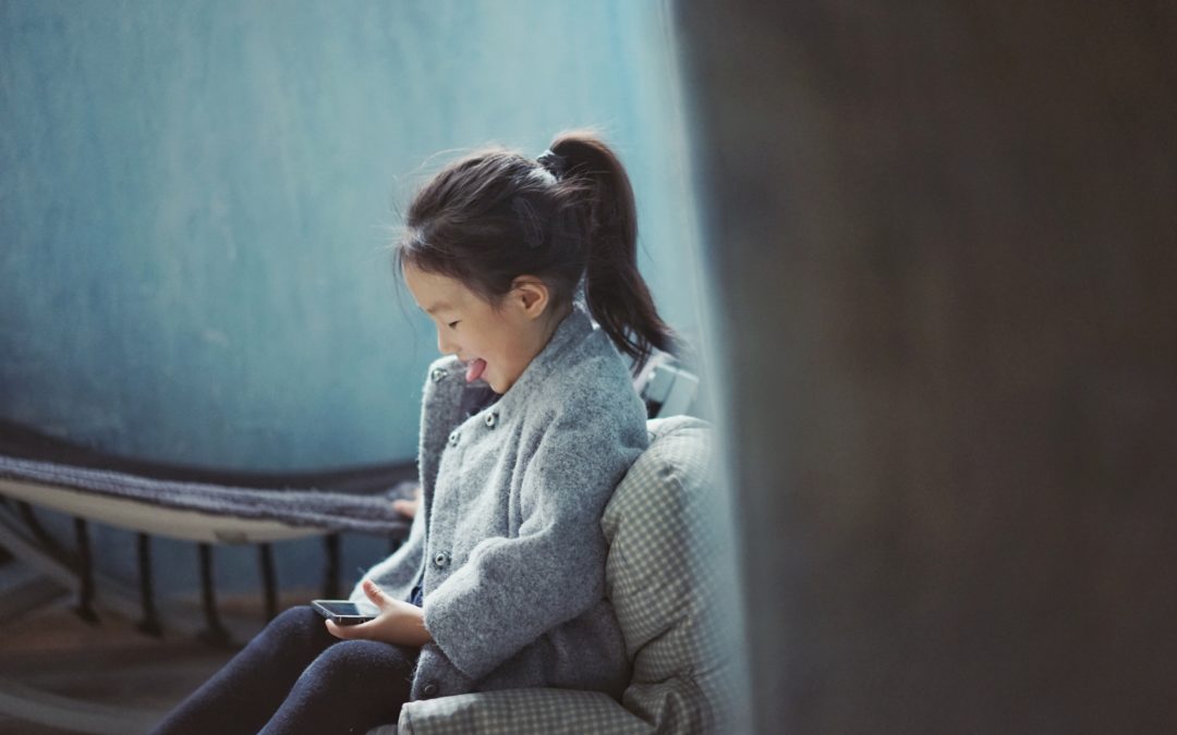 A young girl with a pony tail smiles while looking down at a phone.