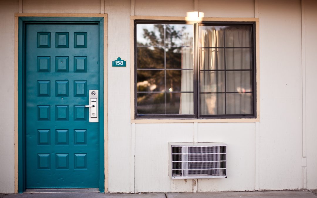 Teal door in a motel on a cream colored wall with a window and AC unit. The number by the door is 158.
