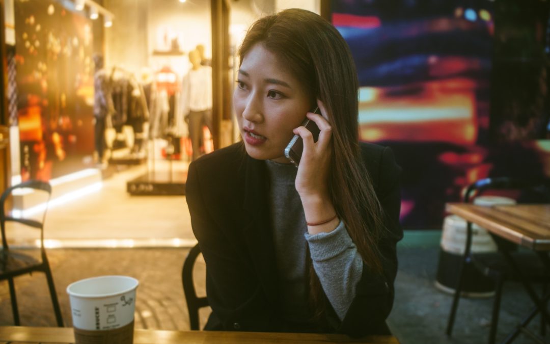 Young Asian woman makes a call on her phone in front of a store in business casual attire