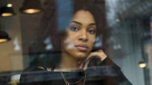 Woman with curly hair looks through a window with head resting on her hand